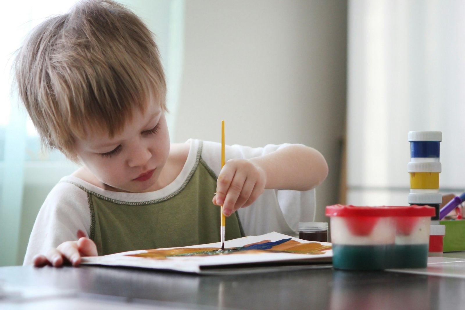 The child paints with a brush on paper. Art therapy.